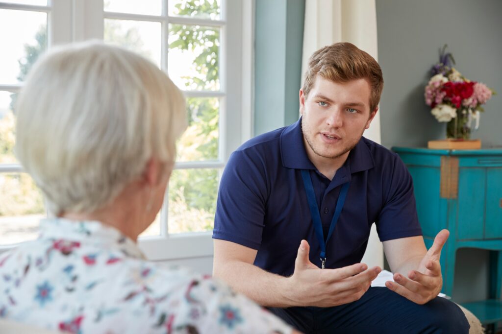 Senior woman talking with male care worker on home visit